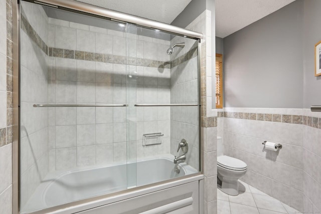 bathroom with tile walls, bath / shower combo with glass door, toilet, a textured ceiling, and tile patterned flooring