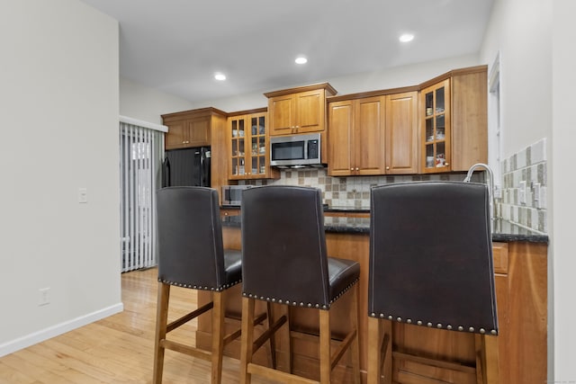 kitchen featuring tasteful backsplash, brown cabinetry, stainless steel microwave, a kitchen breakfast bar, and black refrigerator