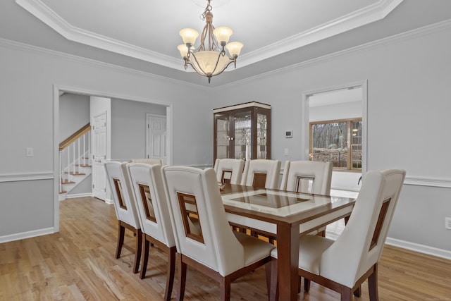 dining area with light wood finished floors, stairs, a tray ceiling, and a notable chandelier