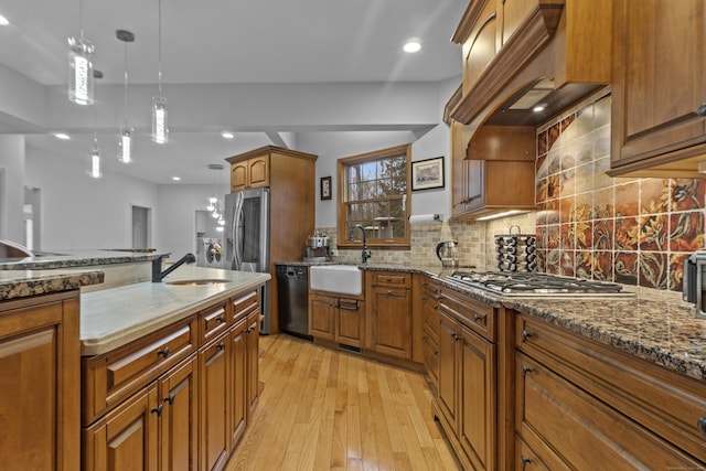 kitchen featuring appliances with stainless steel finishes, backsplash, a sink, and light wood-style flooring