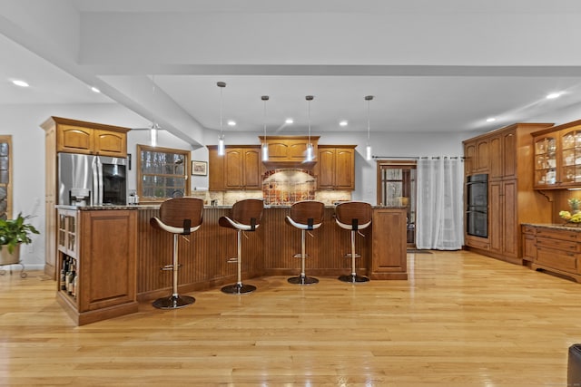 kitchen with light wood-type flooring, stainless steel fridge, and a breakfast bar area