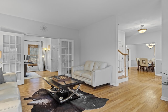 living room featuring a chandelier, baseboards, stairs, french doors, and light wood-type flooring