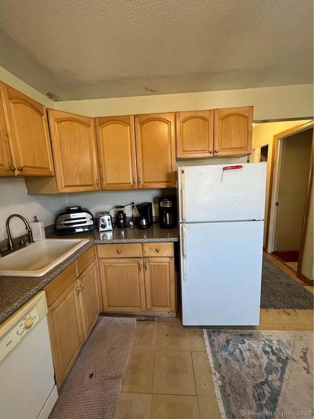 kitchen featuring dark countertops, white appliances, a textured ceiling, and a sink