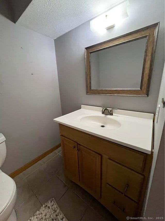 half bath with tile patterned flooring, baseboards, toilet, vanity, and a textured ceiling