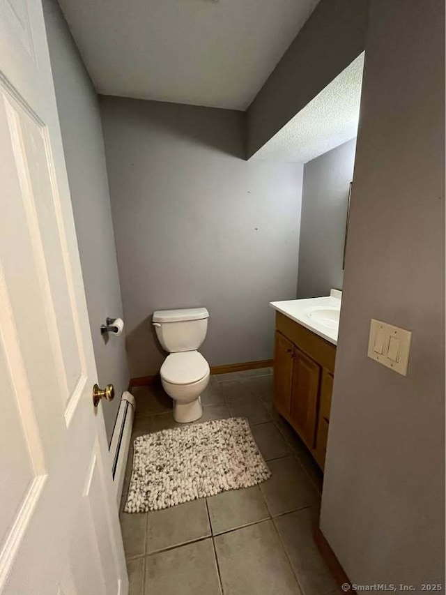 half bathroom with toilet, tile patterned flooring, baseboards, baseboard heating, and vanity