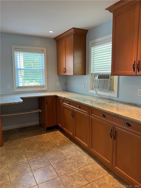 kitchen with built in desk, light stone countertops, light tile patterned floors, and brown cabinets