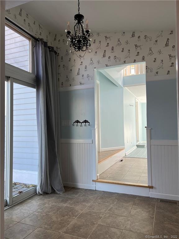 spare room featuring an inviting chandelier, wallpapered walls, and wainscoting