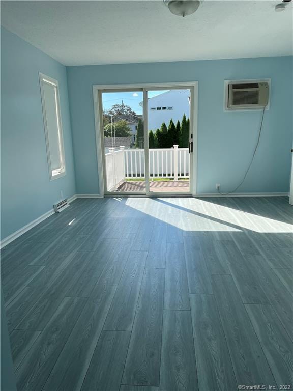 empty room featuring dark wood-style floors, baseboards, and a wall mounted air conditioner