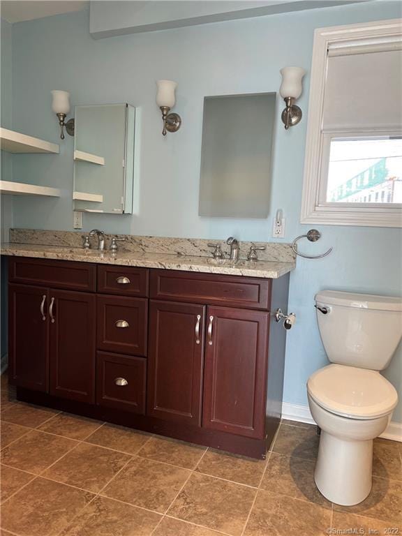 bathroom with toilet, double vanity, a sink, and baseboards
