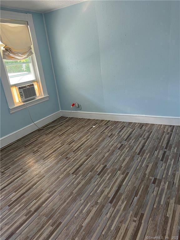 unfurnished room featuring cooling unit, baseboards, and wood finished floors