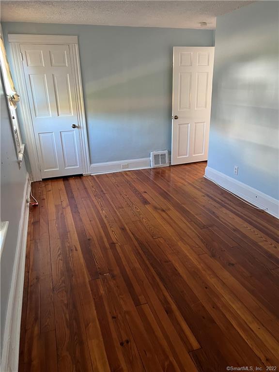 empty room featuring dark wood-style flooring, a textured ceiling, baseboards, and visible vents