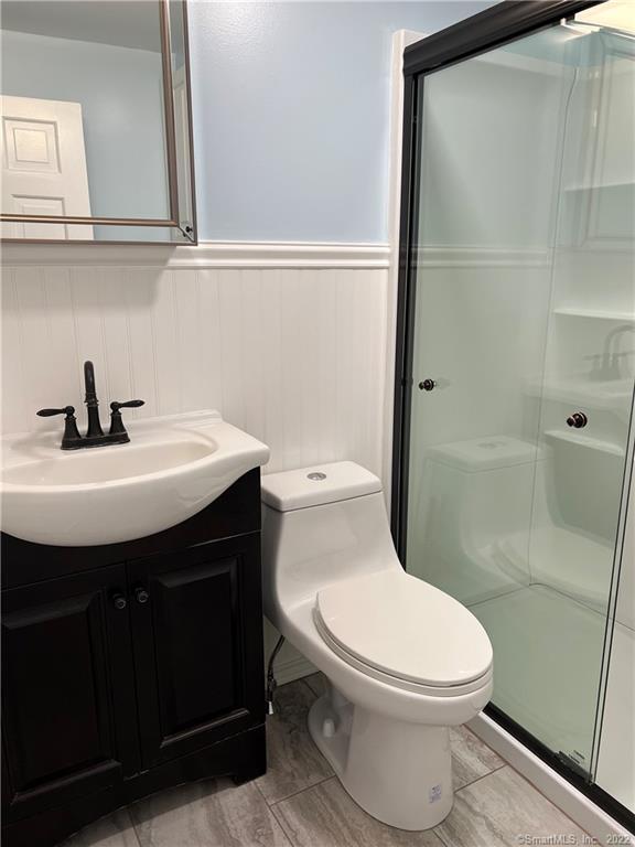 full bathroom featuring toilet, a wainscoted wall, vanity, and a shower stall