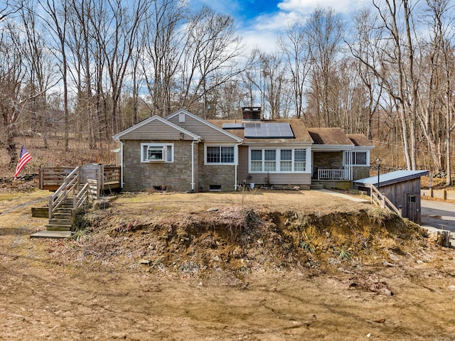 view of front of home with stone siding, roof mounted solar panels, a chimney, and a wooden deck