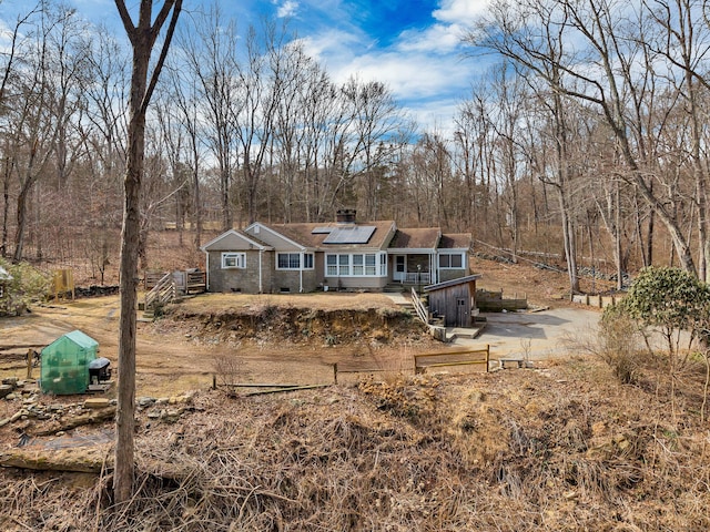 view of front of property with solar panels, a chimney, and a forest view