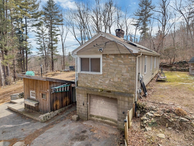 exterior space with a garage, stone siding, a chimney, and concrete driveway