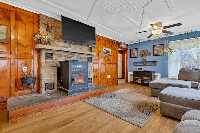 living room with a wood stove, visible vents, a ceiling fan, and wood finished floors