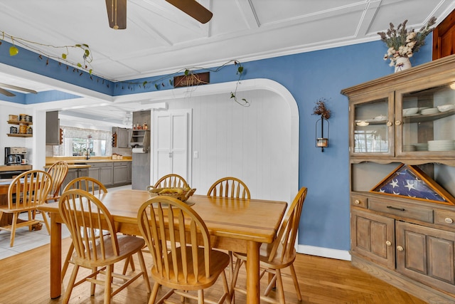 dining room featuring arched walkways, crown molding, ceiling fan, light wood-type flooring, and baseboards