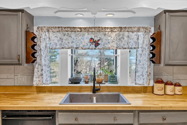 kitchen featuring a sink, butcher block countertops, decorative backsplash, and gray cabinetry