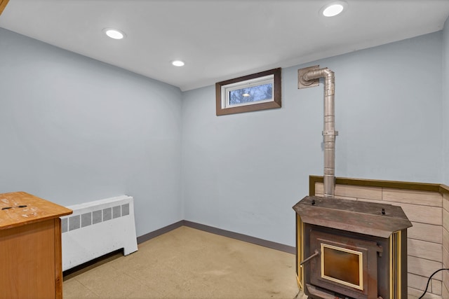 basement with baseboards, radiator, a wood stove, light floors, and recessed lighting