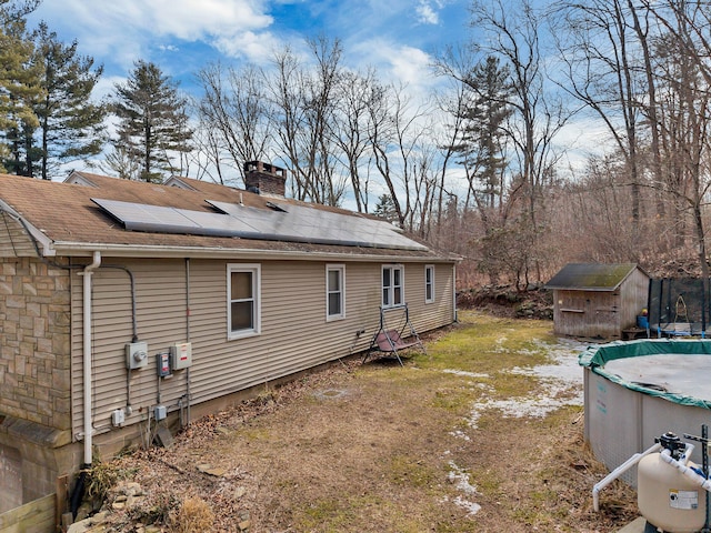 exterior space with a chimney, an outbuilding, a trampoline, a storage unit, and roof mounted solar panels