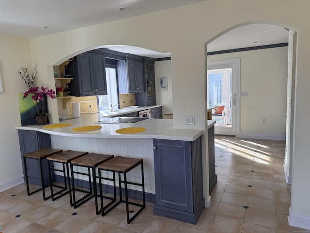 kitchen with a peninsula, a kitchen breakfast bar, light countertops, open shelves, and tasteful backsplash