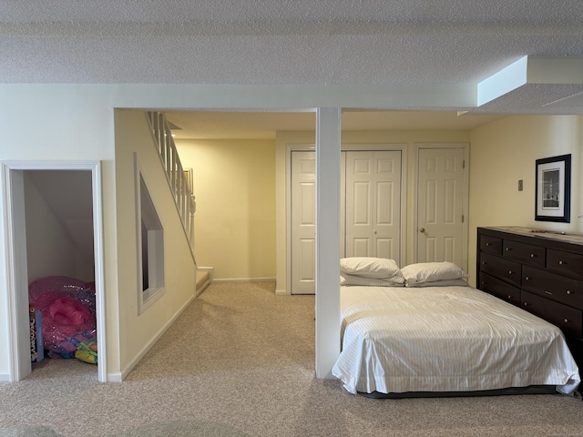 carpeted bedroom featuring a textured ceiling, two closets, and baseboards