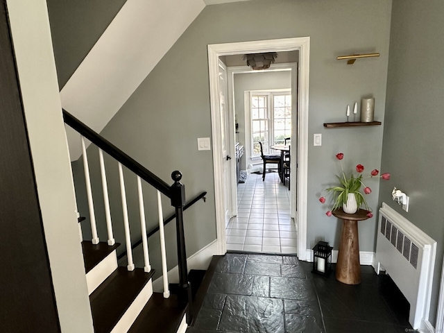 doorway featuring stone tile flooring, baseboards, radiator heating unit, and stairs