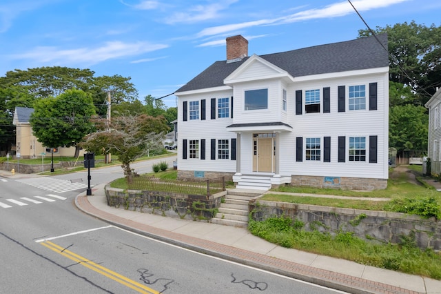 colonial-style house featuring roof with shingles and a chimney