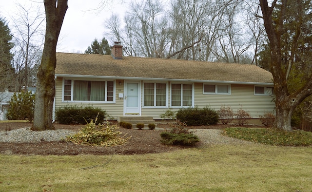 ranch-style home with a shingled roof, a chimney, and a front yard