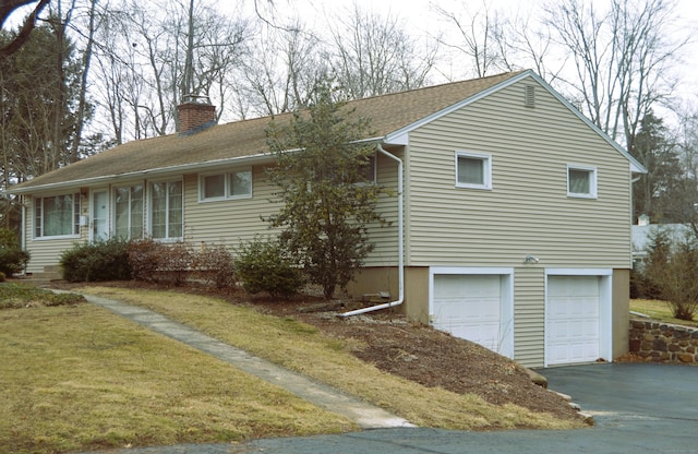 view of front of home featuring a garage, driveway, a chimney, and roof with shingles