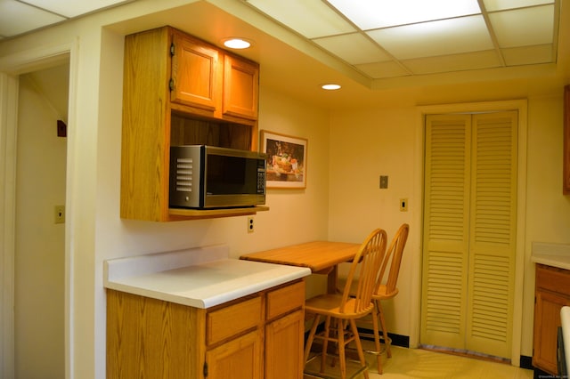 kitchen with a drop ceiling, recessed lighting, light countertops, brown cabinets, and stainless steel microwave