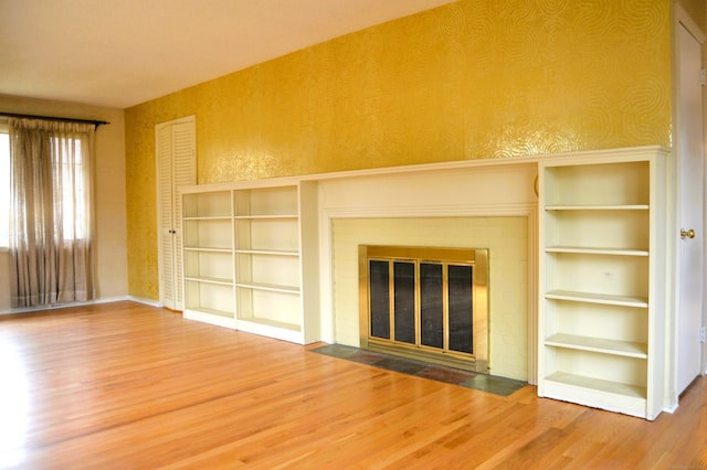 unfurnished living room with wallpapered walls, a fireplace, and wood finished floors