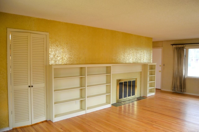 unfurnished living room with a fireplace with flush hearth, wood finished floors, and a textured wall