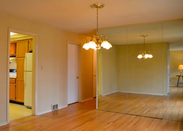 unfurnished room with light wood-type flooring, visible vents, and an inviting chandelier