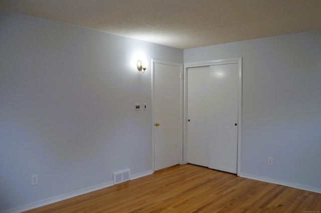 empty room featuring a textured ceiling, baseboards, visible vents, and light wood-style floors