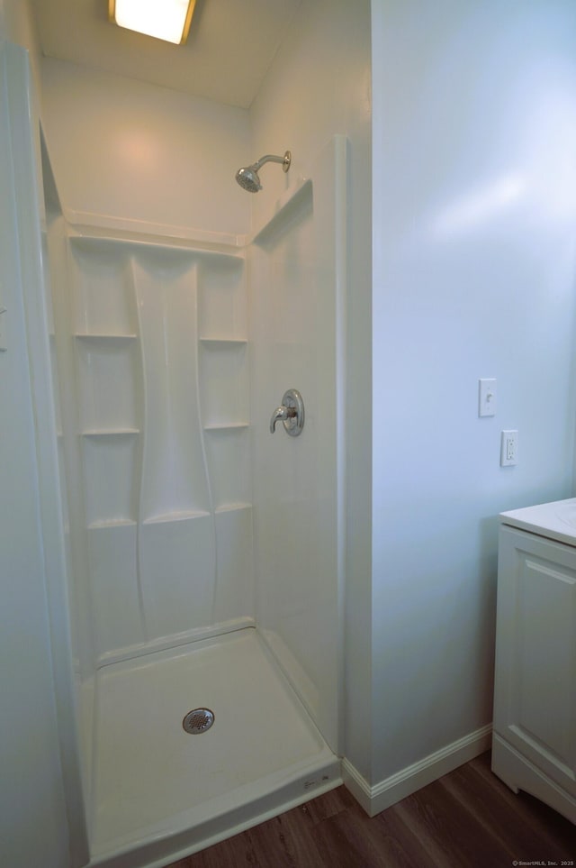 full bath featuring a shower, vanity, baseboards, and wood finished floors