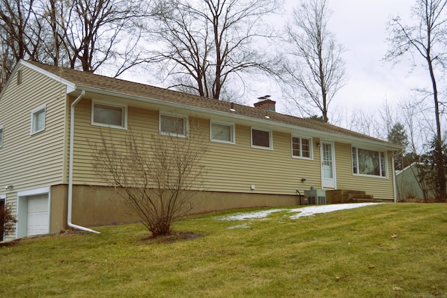 back of house with a garage, a yard, a chimney, and central air condition unit