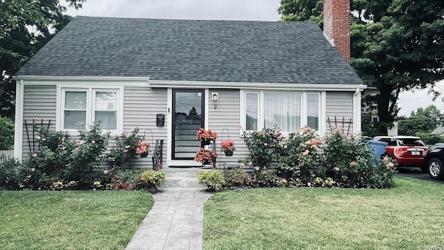 cape cod home featuring roof with shingles, a front lawn, and a chimney