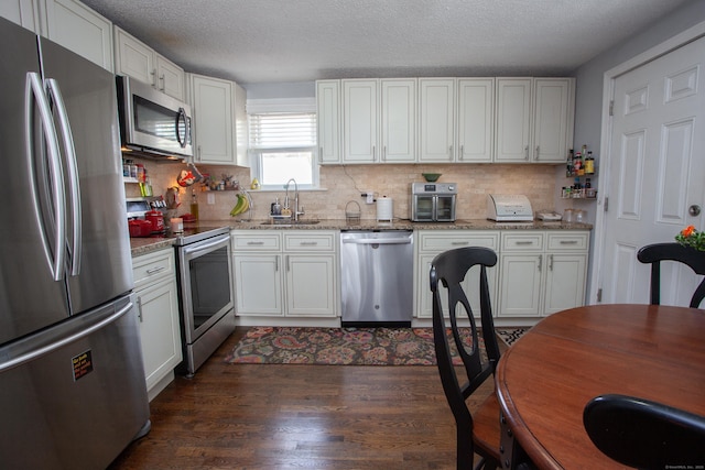 kitchen featuring tasteful backsplash, dark wood-type flooring, light stone countertops, stainless steel appliances, and a sink