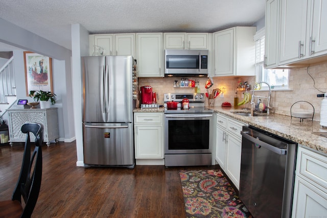 kitchen with dark wood-type flooring, a sink, light stone countertops, stainless steel appliances, and backsplash