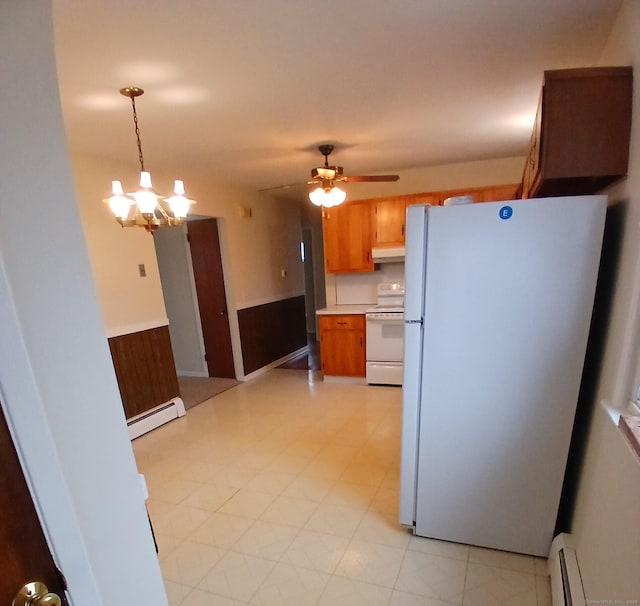 kitchen featuring a wainscoted wall, brown cabinets, a baseboard heating unit, white appliances, and under cabinet range hood