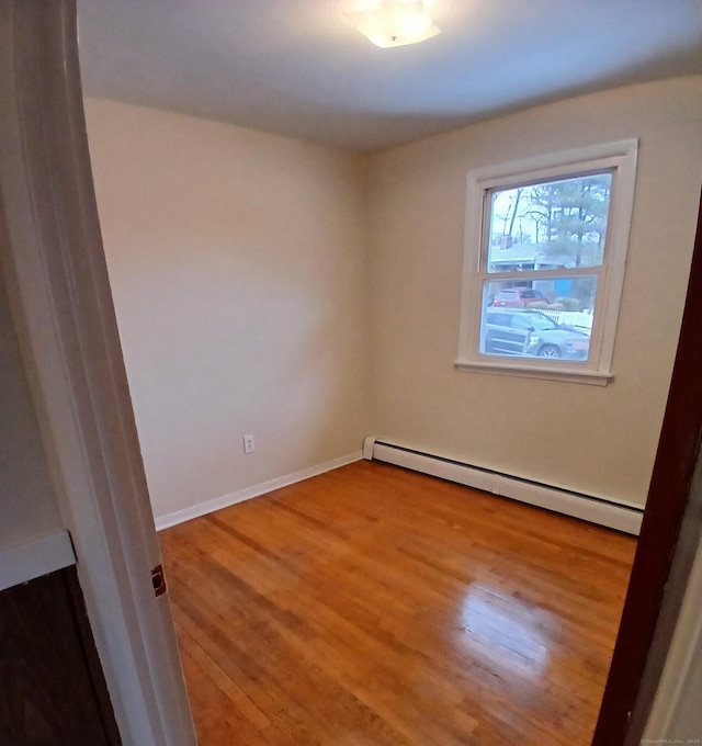 unfurnished room featuring baseboards, baseboard heating, and wood finished floors