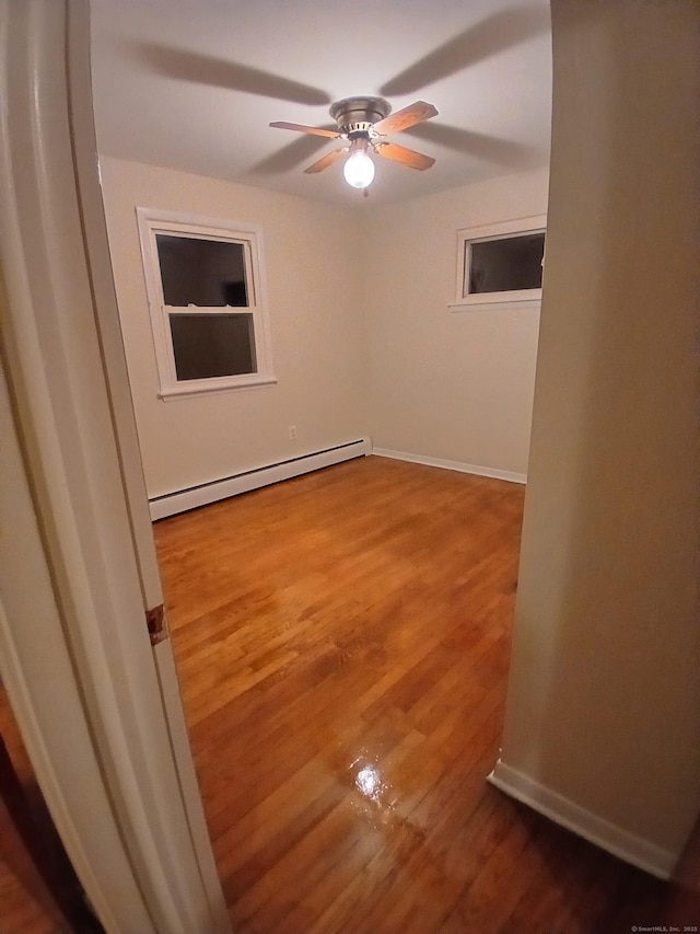 empty room featuring a ceiling fan, baseboards, a baseboard heating unit, and wood finished floors