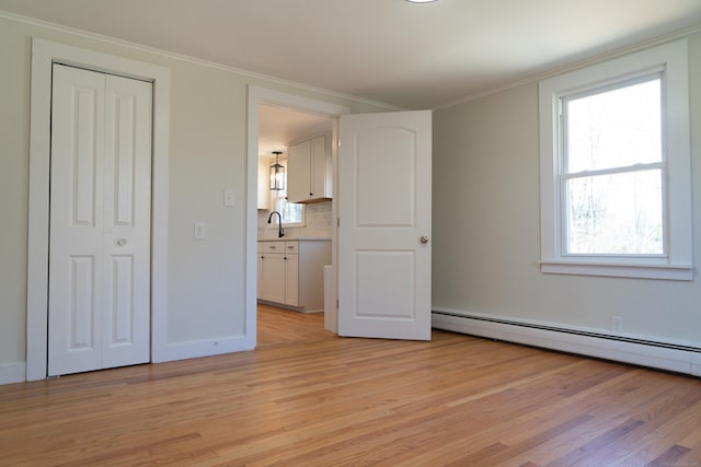 unfurnished bedroom with a closet, crown molding, light wood finished floors, baseboards, and baseboard heating