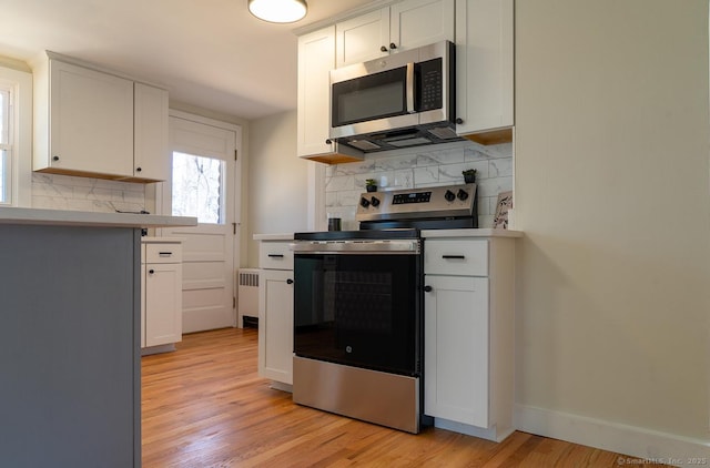 kitchen featuring radiator, light wood finished floors, stainless steel appliances, light countertops, and white cabinetry