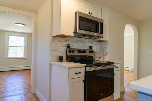 kitchen with tasteful backsplash, arched walkways, appliances with stainless steel finishes, light countertops, and a baseboard radiator