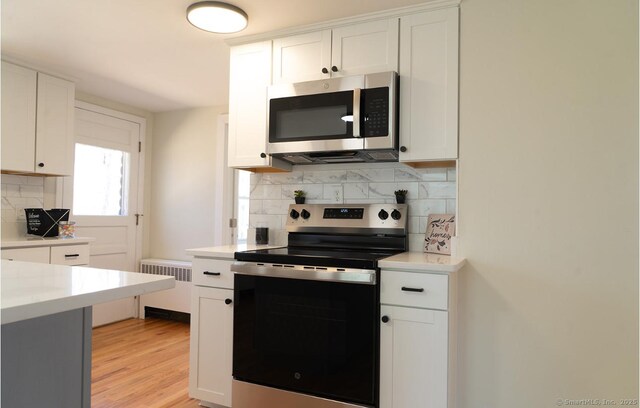 kitchen with white cabinetry, appliances with stainless steel finishes, light countertops, and radiator heating unit