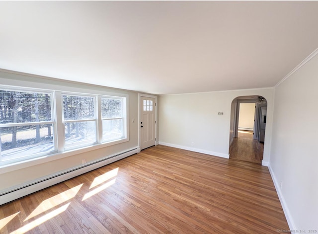 empty room with light wood finished floors, a baseboard heating unit, baseboards, ornamental molding, and arched walkways