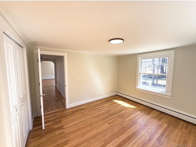 empty room featuring baseboard heating, crown molding, and light wood-type flooring