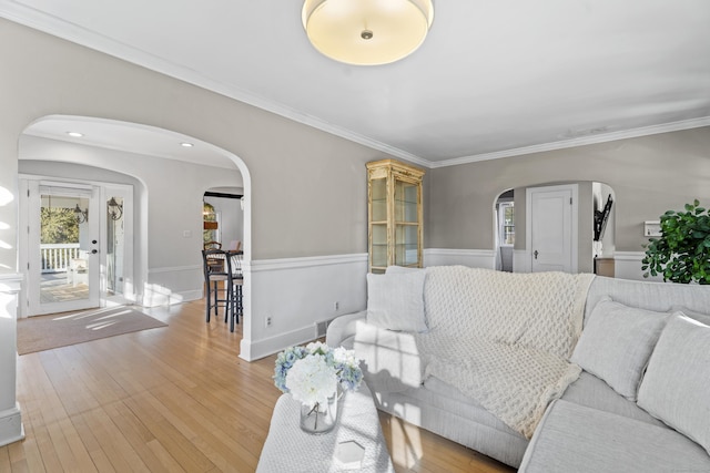 living area featuring arched walkways, crown molding, and light wood-type flooring